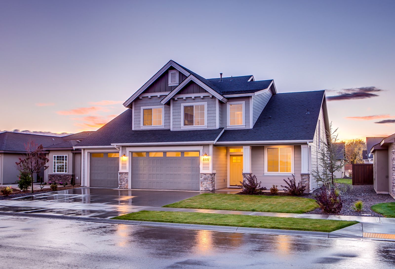 Premium suburban Kansas City home at dusk with a three-car attached garage, warm window glow and a clear evening sky